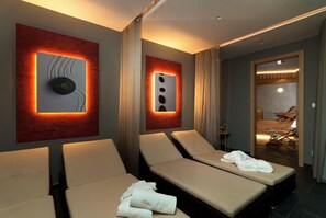 A modern spa room with two massage tables, a wall-mounted massage chair, and a separate room with a massage chair and a wooden floor. - Hotel Grand (Spindleruv mlyn)