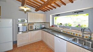 A kitchen with white cabinets, a stainless steel sink, a window with a view of greenery, and a wooden ceiling structure. - Villa Cristiana (Proceno)