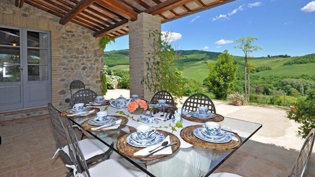 A dining area with a table set for four, stone walls, and a view of rolling hills. - Villa Cristiana (Proceno)