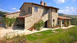 A stone house with a terracotta roof, a staircase leading to a covered porch, and potted plants around the property. - Villa Cristiana (Proceno)