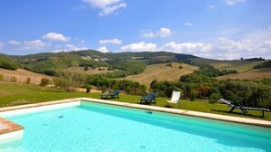 A swimming pool with lounge chairs and a view of rolling hills. - Villa Cristiana (Proceno)