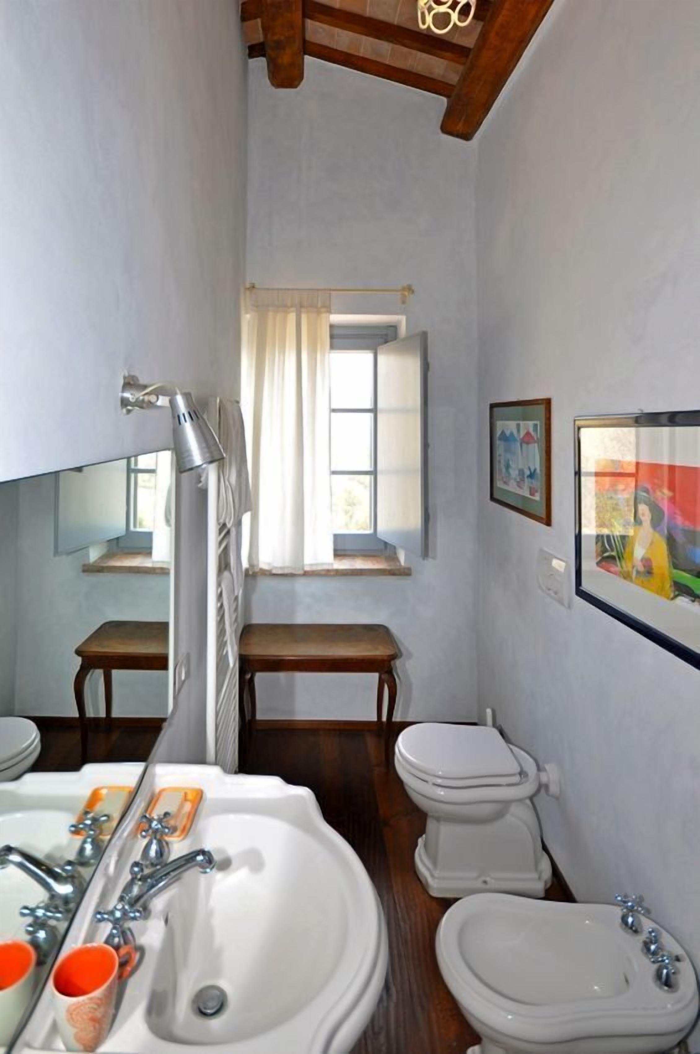 Un baño estrecho con un lavamanos, dos inodoros, una ventana y un espejo.