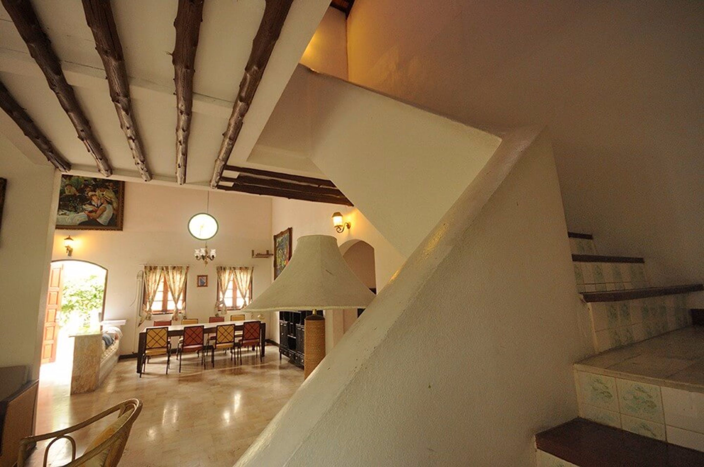 A dining area with a high ceiling and exposed beams, a chandelier, and a view of the kitchen in the background.