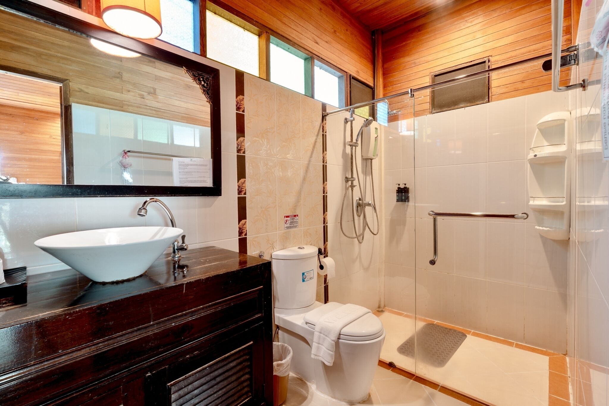 A bathroom with a large mirror, a white sink, a toilet, and a shower area.