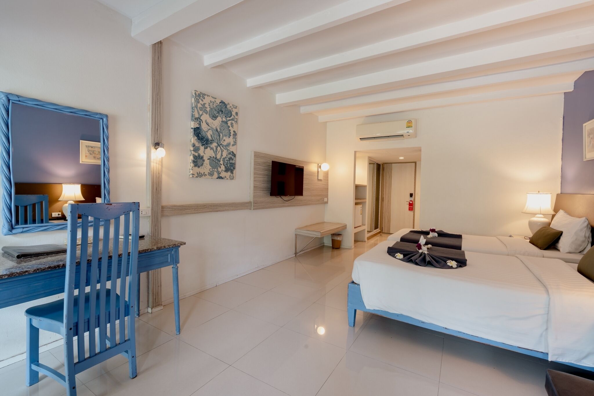 A hotel room with a bed, a desk, a chair, a TV, and a painting on the wall.