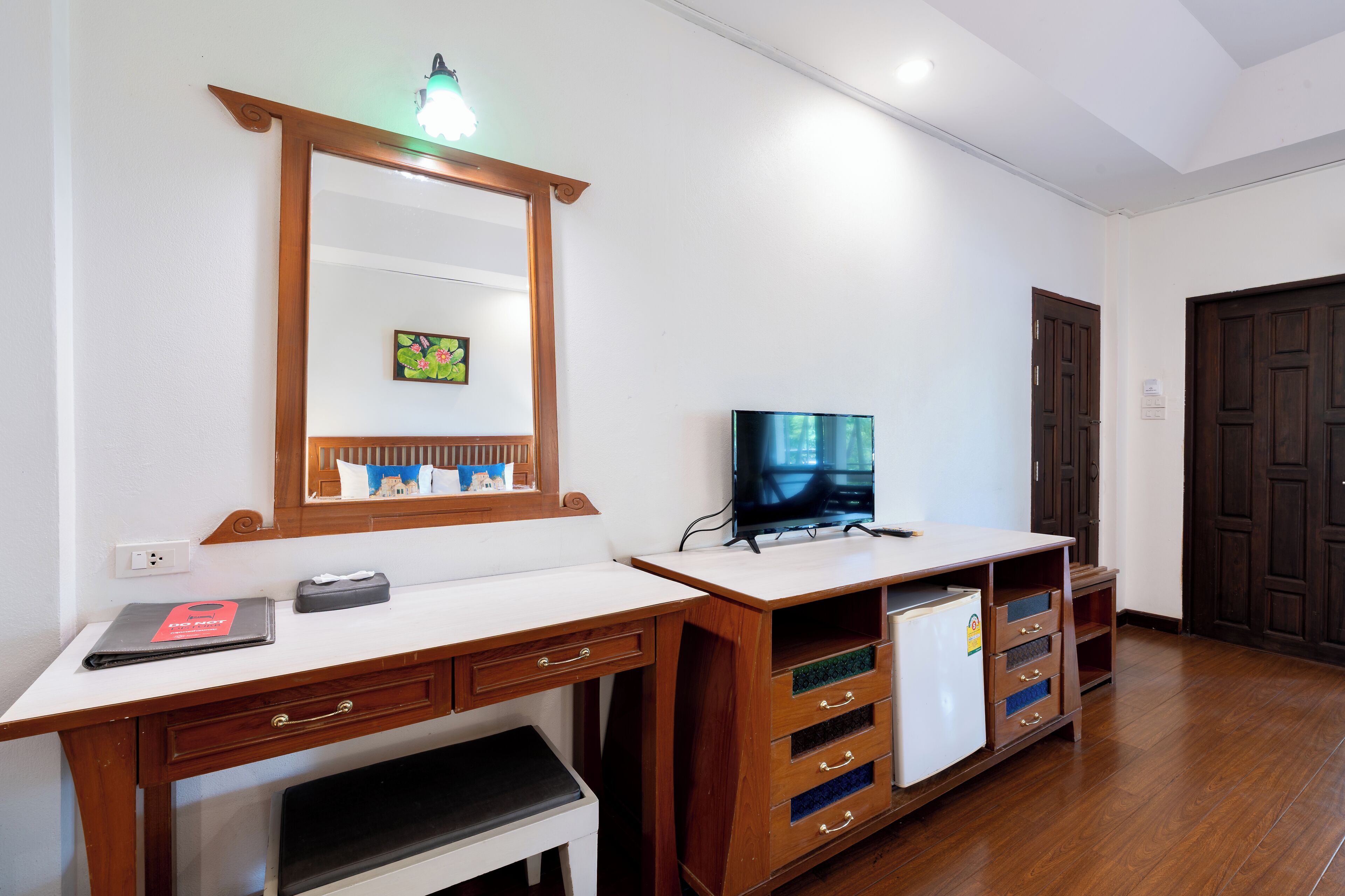 A room with a wooden desk, a television, a mirror, and a refrigerator.