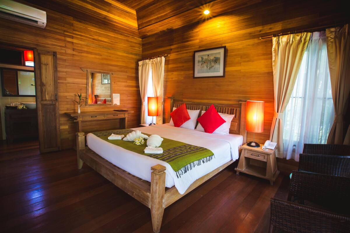 A wooden-floored hotel room with a bed, two bedside lamps, a nightstand, a chair, and a mirror.