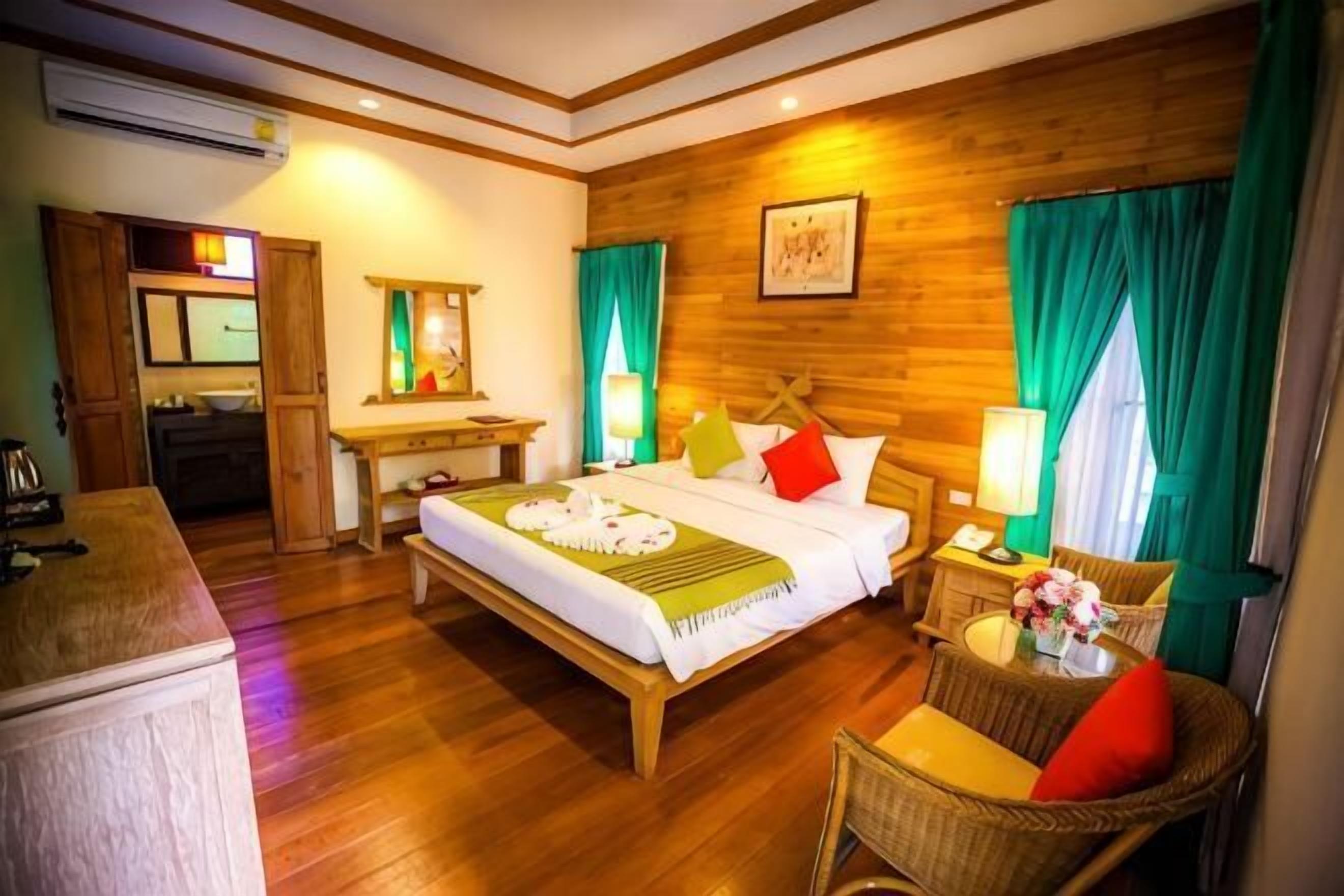 A hotel room with a wooden bed, a desk, a chair, and a small table with a lamp.