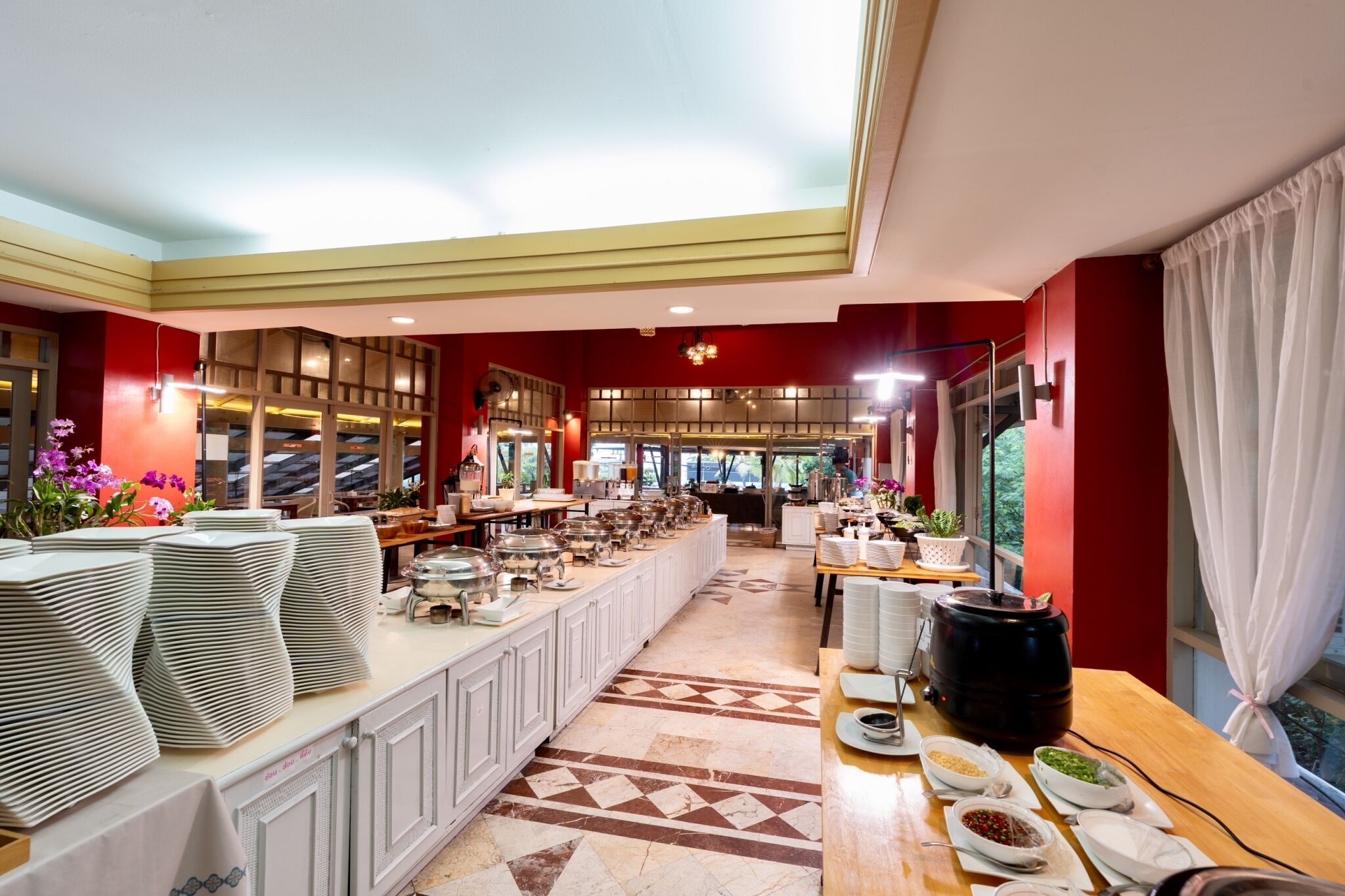 A spacious hotel dining area with a long counter, multiple serving stations, and a variety of food items displayed.