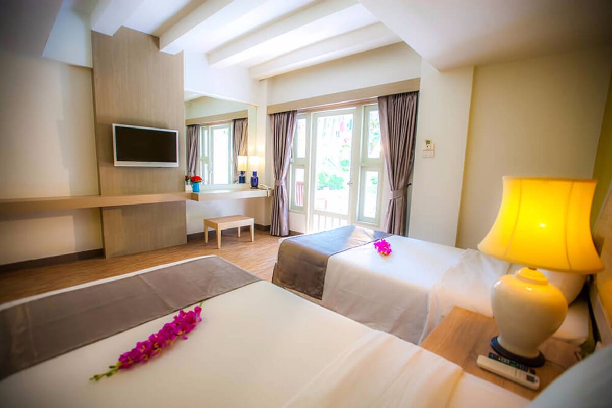 A hotel room with two beds, a TV, a desk, and a lamp.