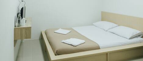 Un dormitorio minimalista con cama de madera, ropa de cama blanca y una mesita de noche con una botella y un vaso.