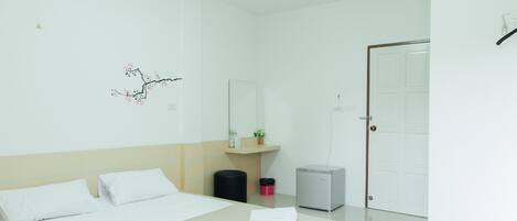 Una habitación de hotel con cama, escritorio pequeño, espejo, cesto de basura y puerta.