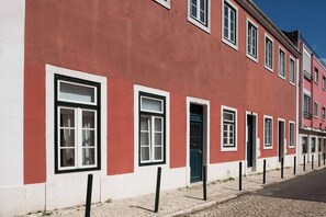 A row of red and white buildings with multiple windows and doors, a cobblestone street, and black bollards. - CASA AMORA Studio Apartments (Lisbon)