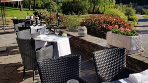 An outdoor dining area with tables and chairs, surrounded by greenery and a view of a hill. - Auberge d'Alle (Vresse-sur-Semois)