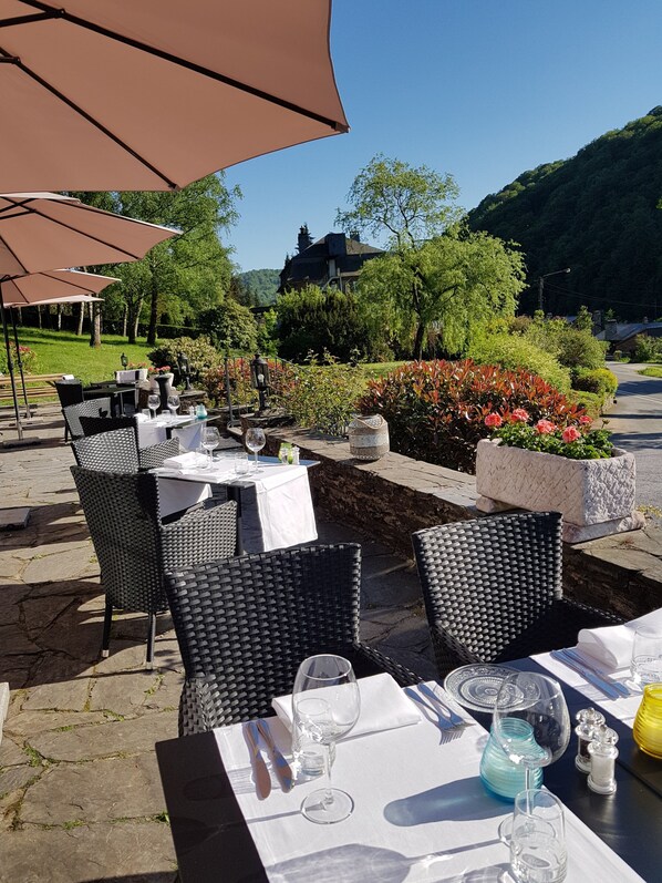 Un área de comedor al aire libre con mesas y sillas, rodeada de vegetación y vistas a una colina.
