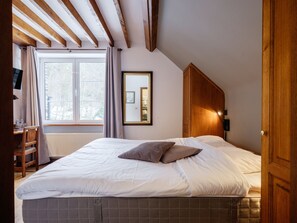 A bedroom with a large bed, wooden ceiling beams, a window with curtains, a desk with a chair, and a wardrobe. - Auberge d'Alle (Vresse-sur-Semois)