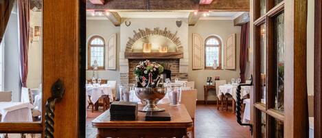 A dining area with a brick fireplace, wooden tables, and chairs.