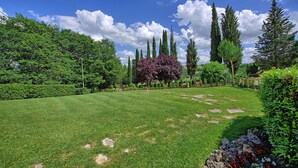 A well-maintained garden with a variety of trees and shrubs, a clear sky, and a paved pathway. - Villa Sabrina (San Gimignano)