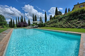 A rectangular swimming pool with clear blue water, surrounded by a well-maintained lawn and various trees. - Villa Sabrina (San Gimignano)