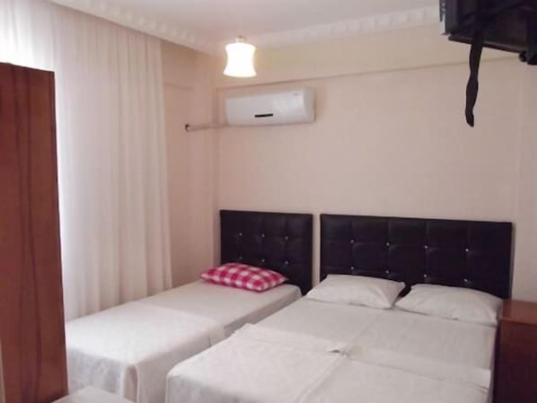 Une chambre d’hôtel avec deux lits simples, un climatiseur blanc, une porte en bois et un luminaire.