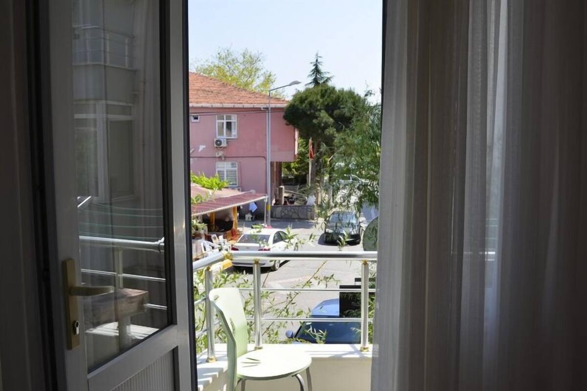 A balcony with a chair, a table, and a view of a street with parked cars and buildings.