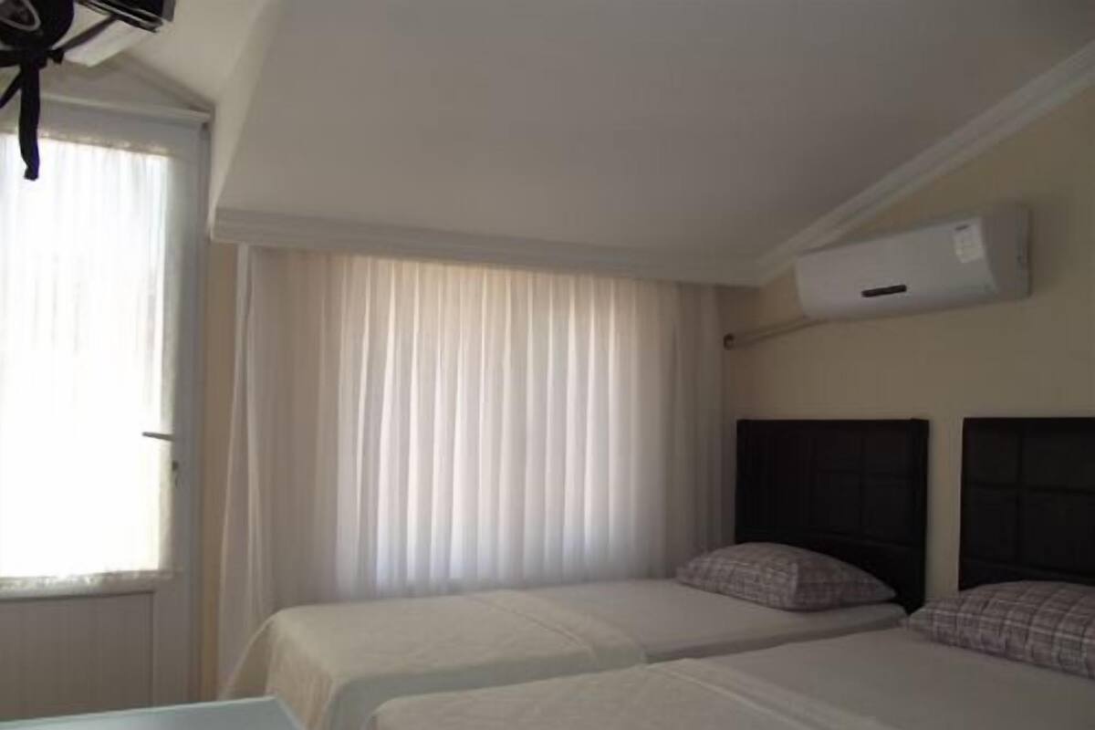 A hotel room with two beds, a window with curtains, an air conditioning unit on the wall, and a table.