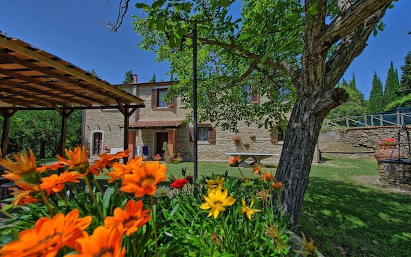 Ein Steinhaus mit einer Holzpergola und einem Baum im Vordergrund.