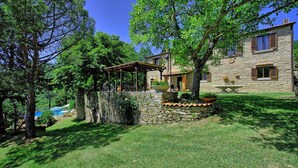 A stone house with a covered patio, a stone wall, and a grassy yard. - Villa Luciano (Arezzo)