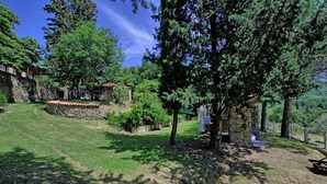 A stone building with a tiled roof, surrounded by lush greenery and trees. - Villa Luciano (Arezzo)