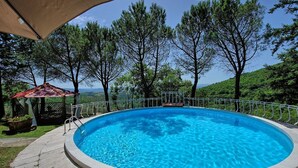 A round swimming pool with a metal railing, surrounded by trees and a gazebo. - Villa Luciano (Arezzo)