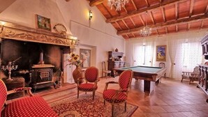 A spacious room with a pool table, red upholstered chairs, a fireplace, and a chandelier. - Villa Luciano (Arezzo)