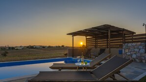 A poolside area with lounge chairs and a table with a bottle and glass, overlooking a pool and a sunset view. - Esperanza Villas (Nea Propontida)