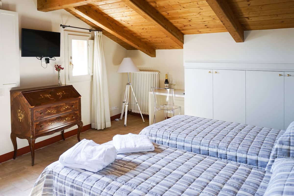 A bedroom with a wooden ceiling, a dresser, a TV, a radiator, and a bed with a blue and white striped duvet.