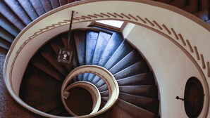 A spiral staircase with a wooden handrail and a metal railing, leading to a landing with a small window. - Casa Isolani Santo Stefano (Bologna)