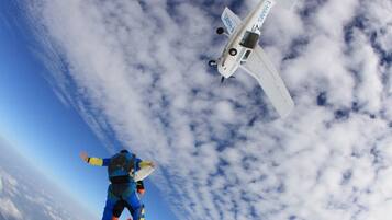 Ein Fallschirmspringer und ein kleines Flugzeug am Himmel.