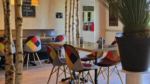 Un espace repas agrémenté de bouleaux, de chaises colorées, d’une grande plante en pot et d’une lampe suspendue.