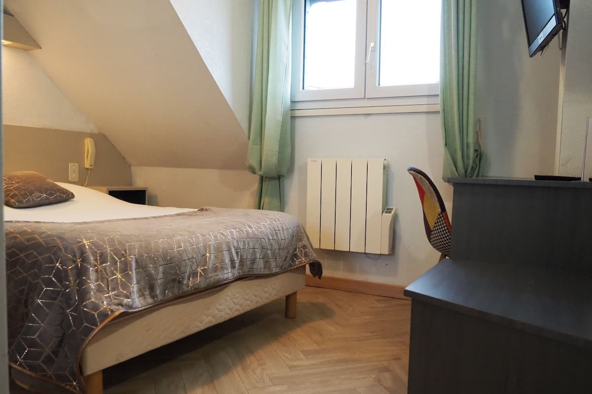 Une chambre à coucher avec un lit, un radiateur, un bureau et une fenêtre avec des rideaux.