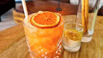 Um copo de suco de laranja com uma fatia de laranja na borda, um copo medidor com líquido amarelado e um copo de água com uma fatia de limão sobre uma mesa de madeira.
