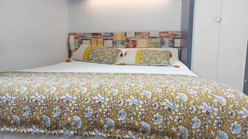 Un lit bien fait, recouvert d’une couvre-lit à motifs floraux et agrémenté de deux oreillers aux motifs jaunes et blancs.