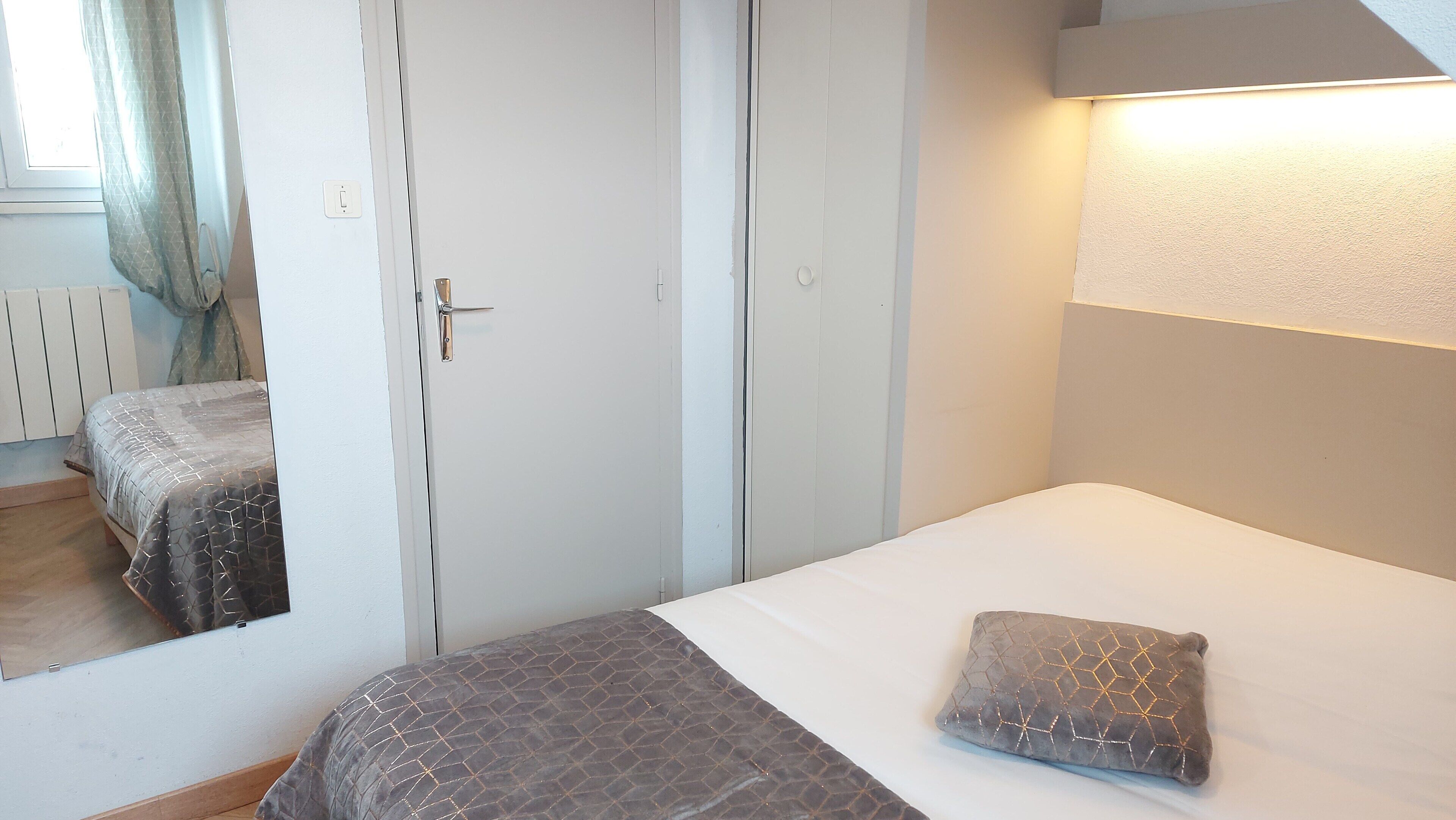 A bedroom with a bed, a bedside table, a lamp, and a mirror.