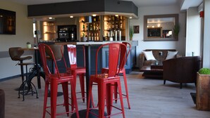 Une cuisine moderne avec un coin bar, des tabourets de bar rouges et un espace salon avec un canapé et des fauteuils marron.
