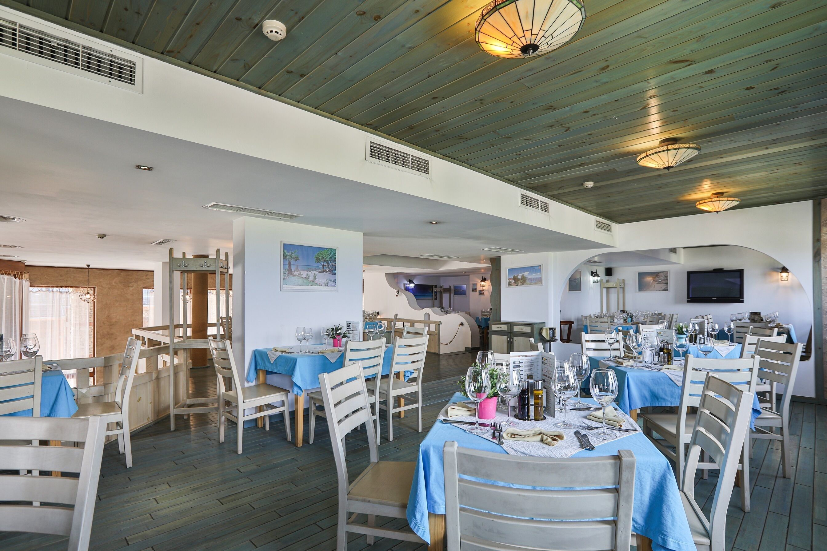 A restaurant with wooden tables and chairs, blue tablecloths, and a wooden ceiling.