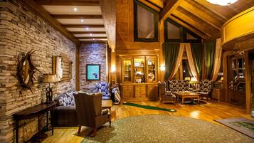 A cozy, rustic interior with exposed wooden beams, a stone wall, and a green patterned rug.