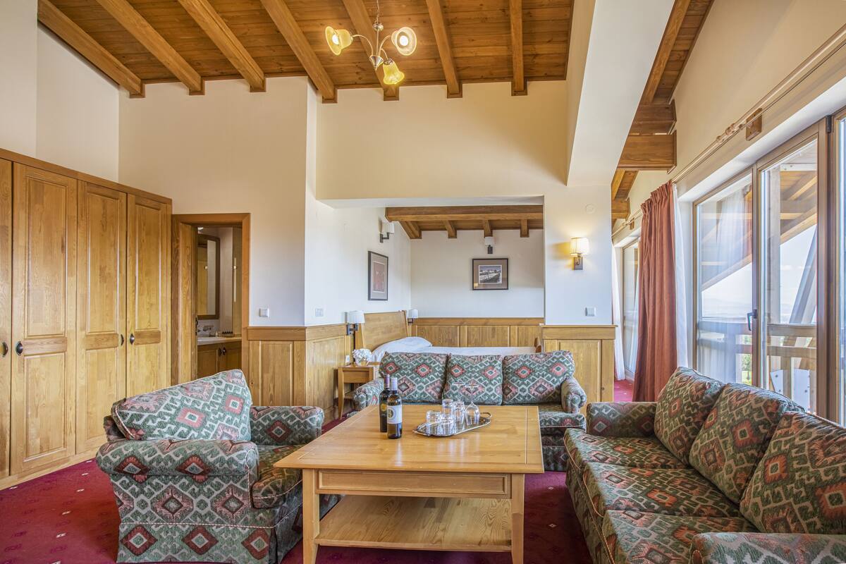 A cozy living room with patterned sofas, a wooden coffee table, and a wooden ceiling.