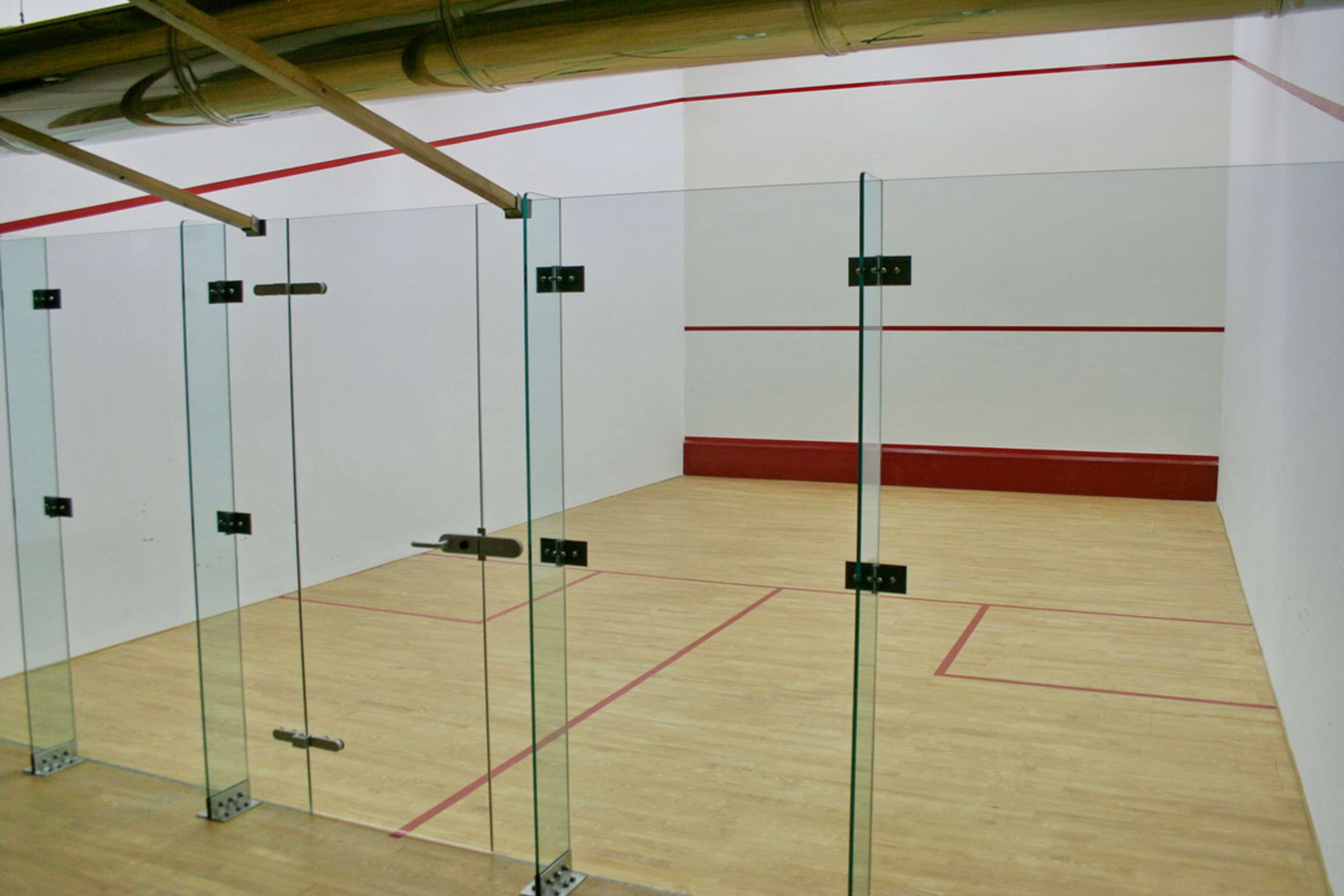 Una cancha de squash con paredes de vidrio y piso de madera.