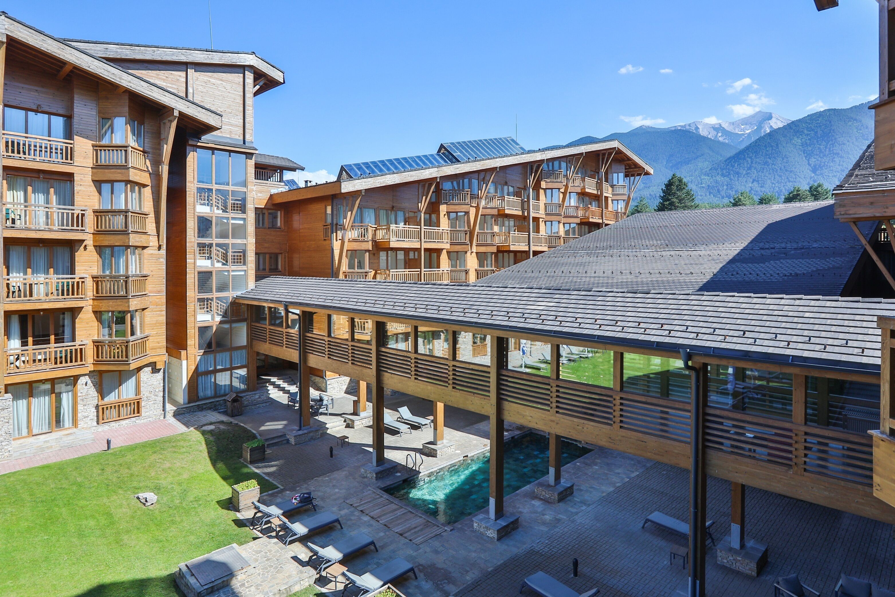 A modern hotel with multiple balconies, a covered outdoor area with seating, and a pool.
