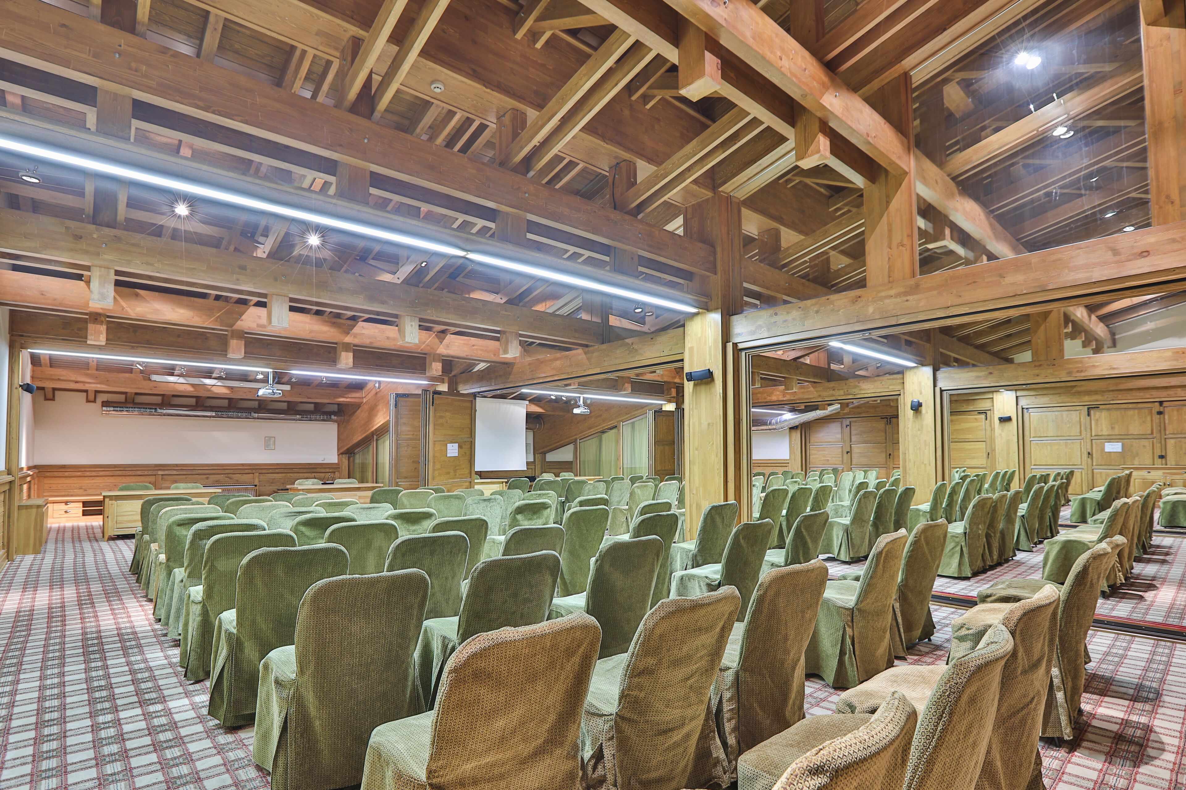A conference room with rows of chairs and tables, wooden beams on the ceiling, and a projector screen.