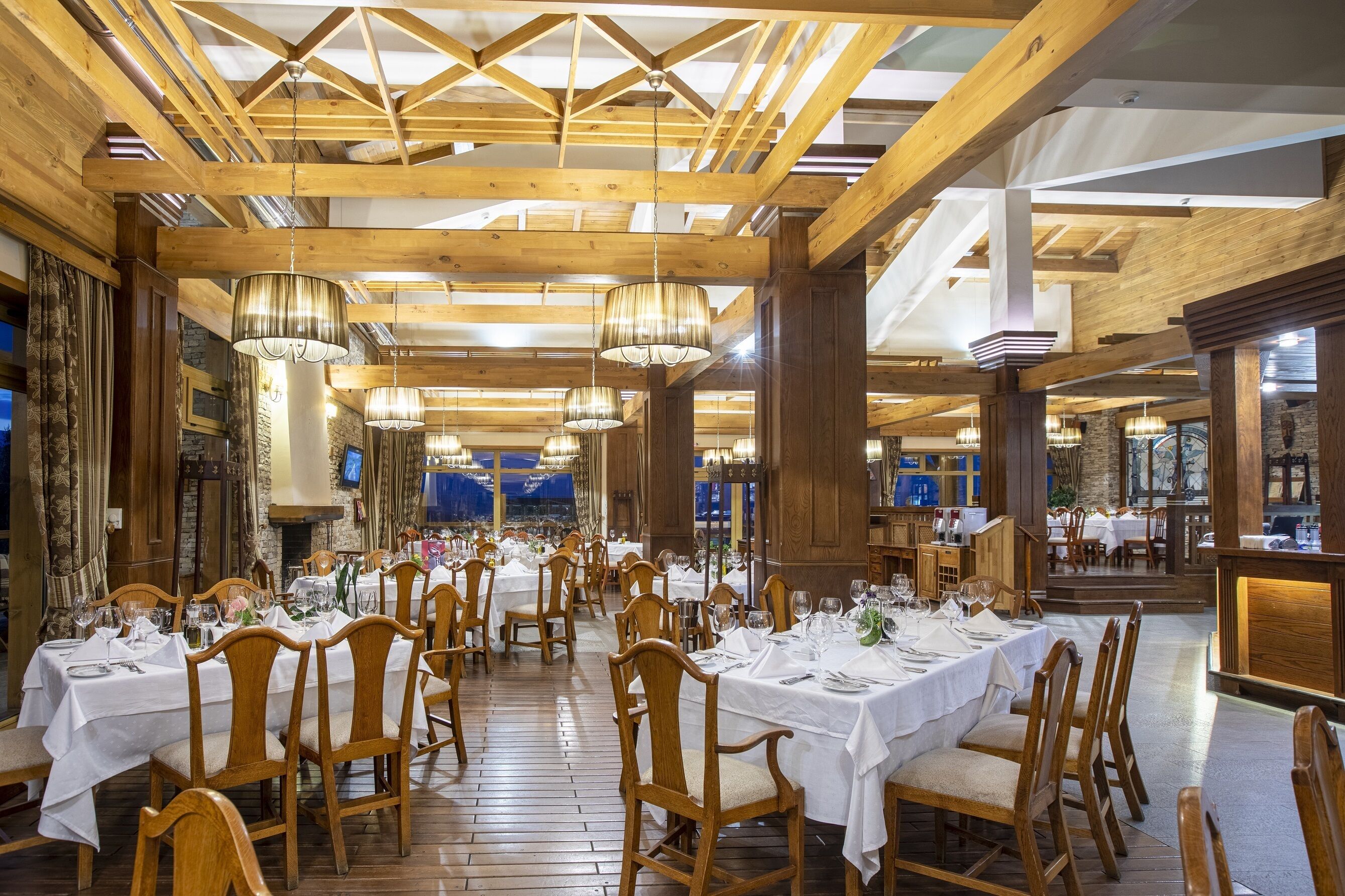 A restaurant with wooden beams, white tablecloths, and chandeliers.