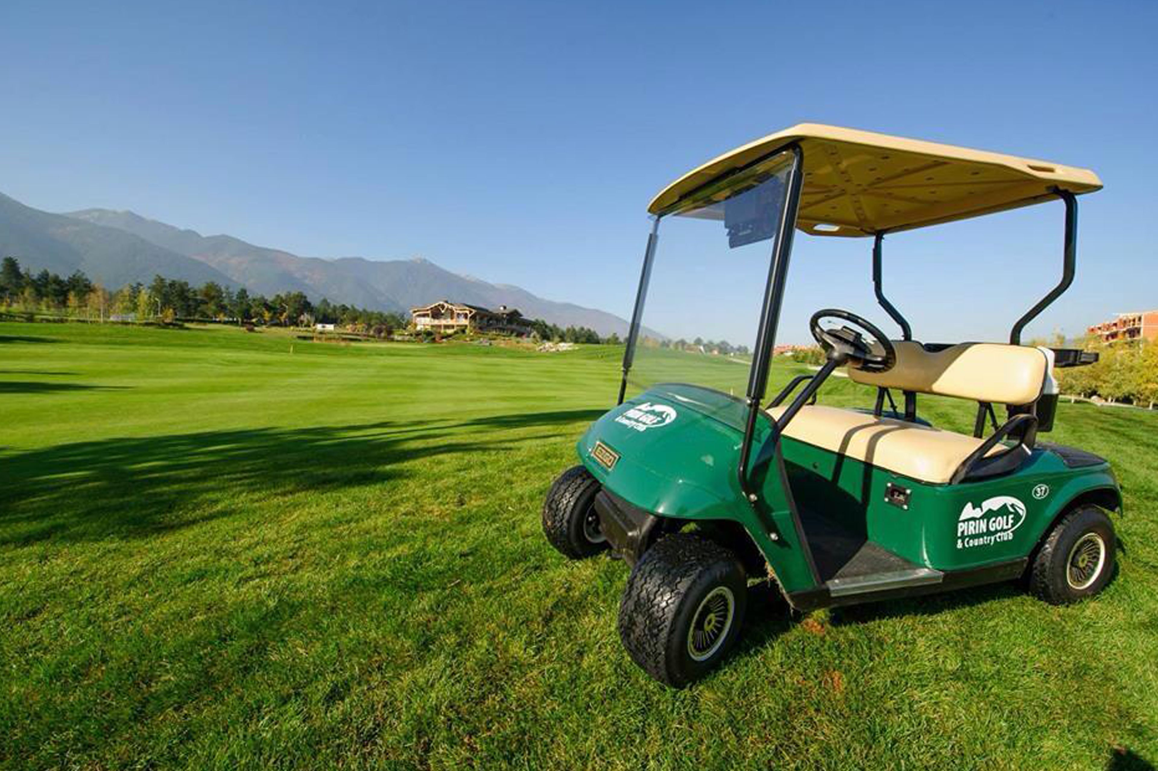 Un carrito de golf en un campo de golf bien cuidado, con cielo despejado y montañas al fondo.