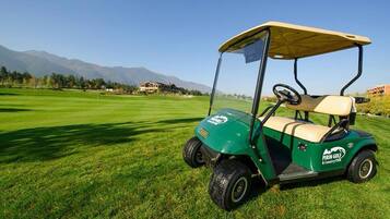 Un carrito de golf en un campo de golf bien cuidado, con cielo despejado y montañas al fondo.